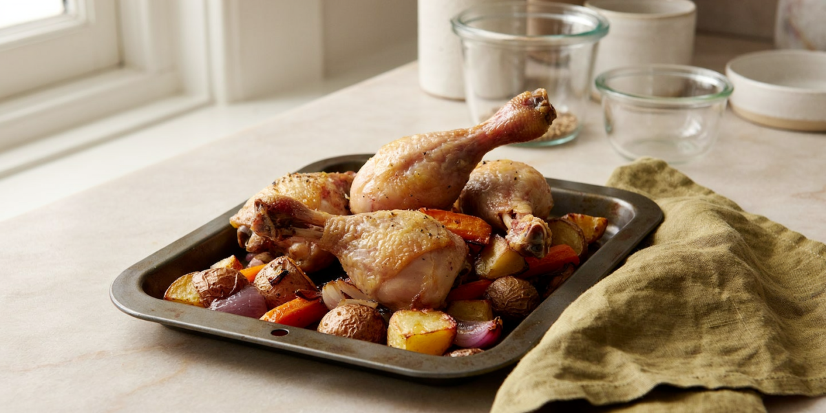 Roasted chicken leg quarters on a sheet pan over potatoes and carrots