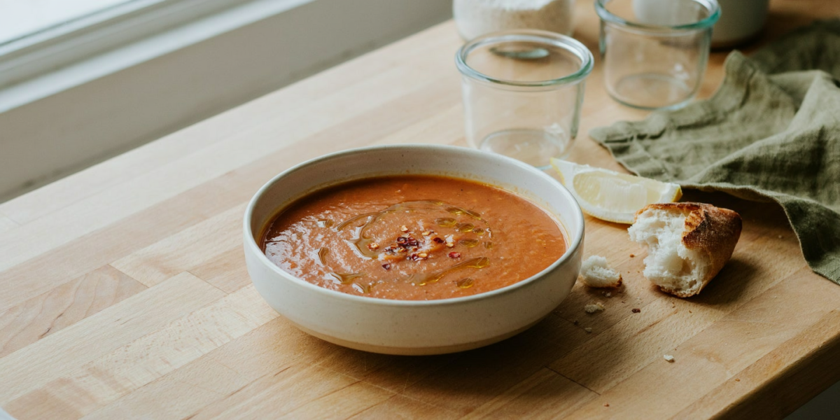 A bowl of orange red lentil soup with lemon and bread