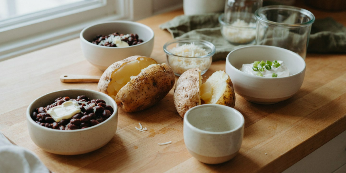 Baked potatoes split open with toppings in small bowls around them