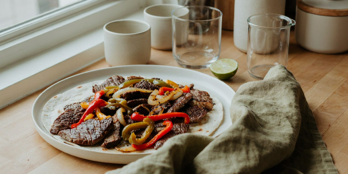 Sliced steak with charred peppers and onions in a skillet with tortillas