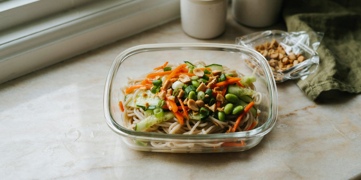 Cold peanut noodles with carrot, cucumber and edamame in a container