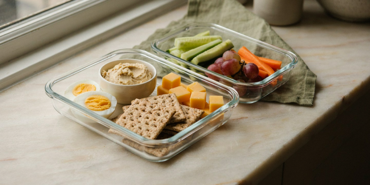 A divided lunch box with hummus, eggs, cheese, crackers and vegetables