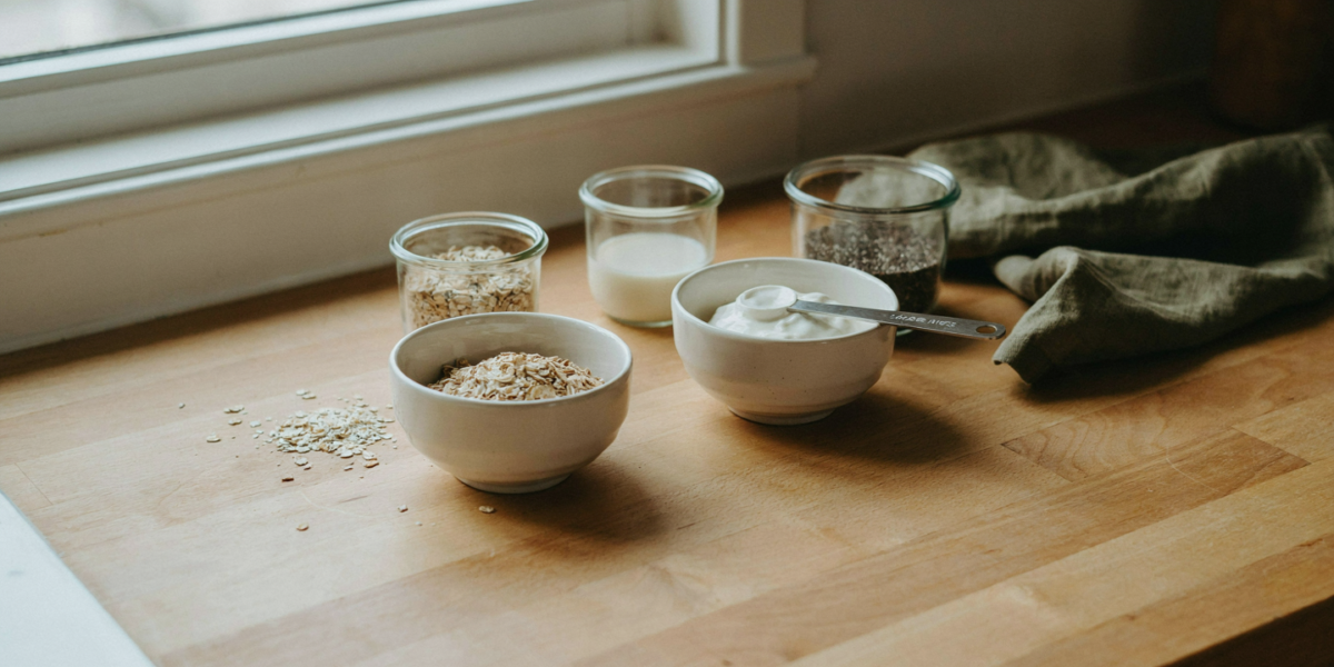 A glass jar of plain overnight oats with oats, milk, yogurt and chia seeds measured out beside it