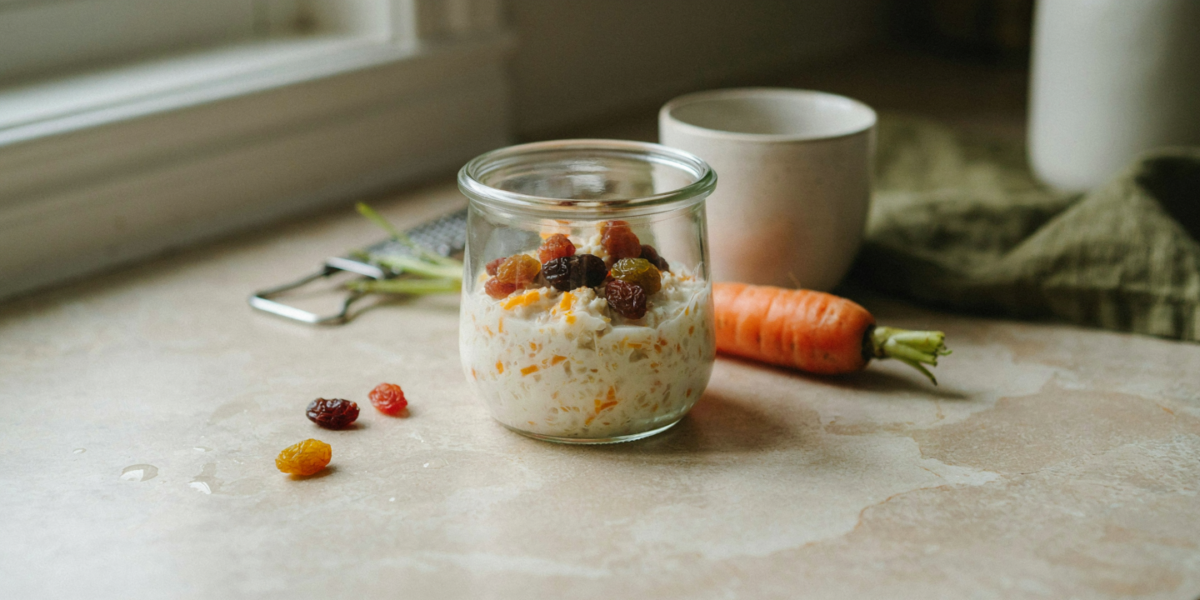 A jar of overnight oats with grated carrot and raisins, a whole carrot and a small grater beside it